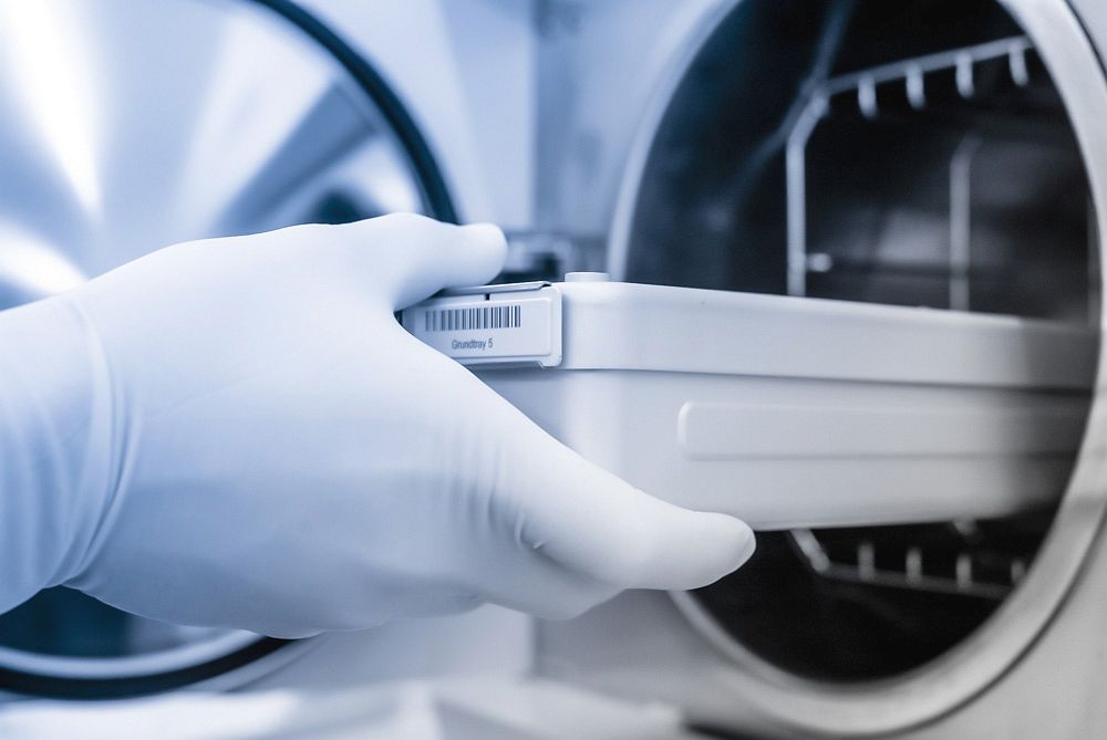 Behandschuhte Hand zieht eine Sterilisationsschublade aus einem Autoklaven im OP-Bereich.